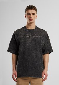 Overdimensioneret sort bomuld t-shirt med en tekstureret overflade og signaturbroderi på brystet. Har en rund halsudskæring og korte ærmer.