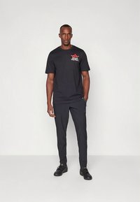 Schwarzes T-Shirt mit rotem "Adidas Football"-Logo, kombiniert mit passenden schwarzen Hosen und schwarzen Sportschuhen. Einfaches Design, atmungsaktiver Stoff.