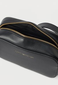 Neceser cosmético de cuero negro con cremallera dorada. Presenta un logotipo grabado en relieve en el frente y una base plana para mayor estabilidad.