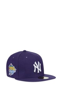 Lila Baseballkappe mit dem weißen Logo der New York Yankees vorne und einem mehrfarbigen "1999 World Series"-Aufnäher an der Seite.