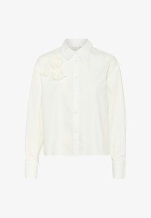 Camicia bianca con colletto a punta, caratterizzata da accenti di rose in tessuto sulla spalla sinistra e maniche lunghe, con una texture liscia.