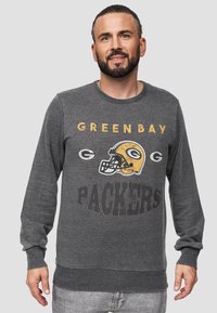 Felpa grigia con colletto rotondo, con la scritta "GREEN BAY PACKERS" e un'illustrazione di un casco in oro e bianco. Tessuto morbido con polsini a coste.