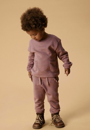 Light pink sweatshirt with two front pockets, matching sweatpants, and brown lace-up boots. Soft texture, casual design, with gathered cuffs.