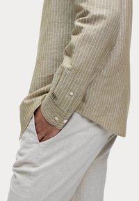 Gestreepte linnen blouse in lichtbeige met witte verticale strepen, met een knoopmanchet en een relaxte pasvorm, gecombineerd met lichtgekleurde broeken.