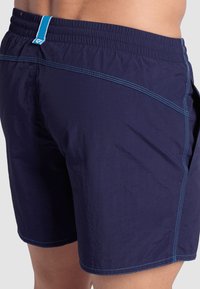 Bañador azul marino con costuras en un tono azul claro. Cuenta con una cintura elástica y un lazo en la parte trasera para colgar.