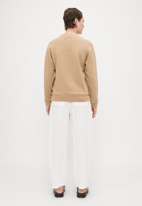 Sweatshirt beige com decote redondo e punhos canelados, combinado com calças brancas soltas e texturizadas, além de sapatos plataforma pretos. Vista traseira.