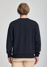 Sudadera de algodón azul marino con mangas largas, puños y dobladillo acanalados. Presenta un cuello redondo y una tela suave y texturizada. Vista trasera lisa.