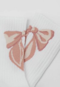 Hvide ribbede sokker med et strikket pink sløjfedesign. Sløjfen har lagdelte sektioner med en glat tekstur og subtile farvegradienter.