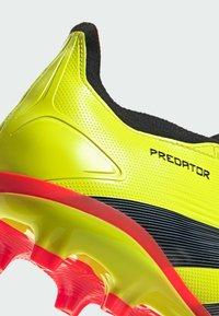 Scarpa da calcio gialla brillante con tomaia texture, accenti neri e suola rossa con tacchetti arrotondati. "PREDATOR" stampato sul lato.