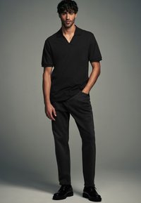 Polo shirt nera a maniche corte con colletto rilassato. Abbinata a jeans scuri e scarpe nere stringate, presenta un design semplice ed elegante.