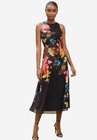Kukkakuosi mekko, jossa on istuva bodice ja levenevä hame mustassa kankaassa, värikkäillä kukilla ja perhosilla, yhdistettynä mustiin korkokenkiin.