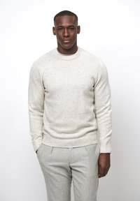 Hellbeige Strickpullover mit gesprenkelter Textur, Rundhals und gerippten Bündchen, kombiniert mit hellgrauen, taillierten Hosen.