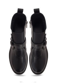Bottes noires en cuir jusqu'à la cheville avec des côtés élastiques, présentant une boucle décorative sur la tige et une texture lisse et polie. Détail de fermeture éclair.