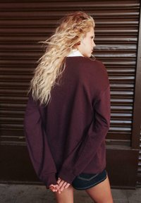 Bordeaux oversized sweatshirt med lange ærmer, rund halsudskæring og struktureret stof, parret med mørke denimshorts mod en brun baggrund.