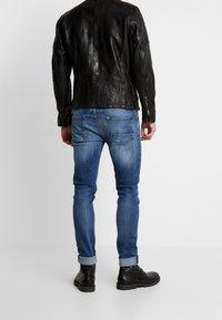 Svart läderjacka med strukturerad yta, kombinerad med ljusblå, smala denimjeans. Svarta ankelstövlar med snörningsdesign.