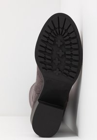 Bota de tobillo de ante marrón con una suela de goma con patrón, que presenta un tacón negro liso y una etiqueta de talla marcada con "37".