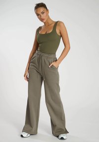 Olivgrünes, figurbetontes Tanktop kombiniert mit lockeren, grauen Sweatpants. Die Hose hat einen elastischen Bund mit Kordelzug und Seitentaschen.