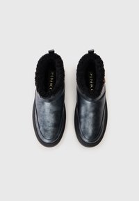Fekete bőr slip-on cipő pár vastag fekete szőrme béleléssel, kerek orral és látható "PINKO" logóval a belsejében.