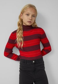 Sweter z długim rękawem, z golfem, w poziome czerwone i burgundowe paski oraz strukturalnym ściągaczem, połączony z czarnymi spodniami z wysokim stanem.