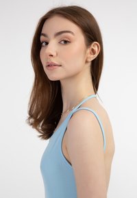 Top fără mâneci, de culoare bleu deschis, cu un model striat, cu bretele subțiri, având un decolteu rotund și un design fără spate, asortat cu un colier delicat din aur.