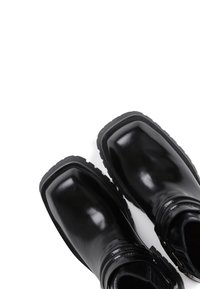 Botas de tobillo negras de cuero pulido con punta cuadrada, suela texturizada y detalle decorativo de correa envolvente.