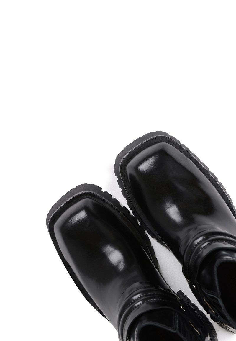 Schwarze Knöchelstiefel aus glänzendem Leder mit rechteckiger Zehenform, strukturiertem Laufsohle und dekorativem Wickelgurt-Detail.