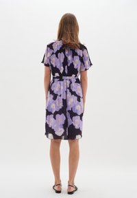 Pleatdress, jossa on violetteja ja laventelinvärisiä kukkakuoseja mustalla taustalla, lyhyet liehuvat hihat ja vyötäröllä vyö.