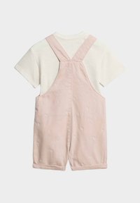 Salopette di cotone rosa con motivi di palme ricamati, caratterizzata da una t-shirt bianca a maniche corte sotto e spalline regolabili.