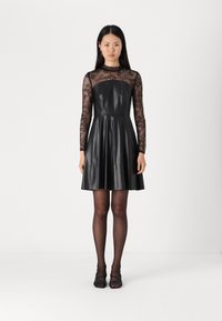 Robe noire avec un corsage ajusté, des manches longues en dentelle, une jupe évasée et une texture lisse semblable au cuir.