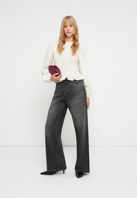 Top bianco a maniche lunghe con texture e maniche a palloncino, abbinato a jeans wide-leg grigi scuri a vita alta e tacchi neri a punta. Tiene una pochette bordeaux.