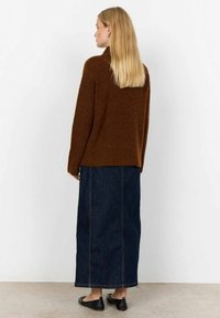 Brun stickad tröja med ett texturerat mönster, kombinerad med en lång mörk denimkjol. Svarta platta skor kompletterar outfiten.