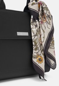 Czarna syntetyczna torebka z srebrną tabliczką z logo, uzupełniona jedwabnym szalikiem w kwiatowy wzór. Gładka tekstura i uporządkowany kształt.