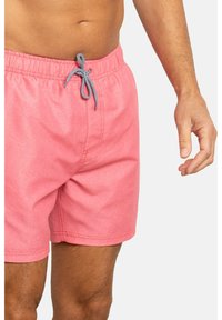 Bañador rosa con cintura elástica, que presenta un cordón de ajuste a rayas negras y blancas. Material suave con un acabado ligeramente texturizado.