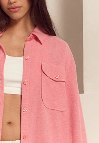 Roze geweven shirt met een knoopsluiting aan de voorkant, een enkele borstzak en een klassieke kraag. Gladde textuur, iets oversized pasvorm.
