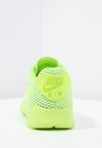 Neon green Nike Air sneaker with mesh upper, shown from the rear on a white surface and background.