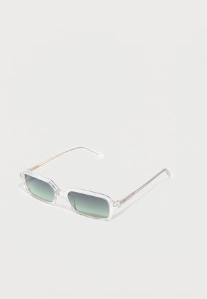 Gafas de sol rectangulares transparentes con lentes tintados en verde, varillas finas y claras, apoyadas sobre una superficie blanca.