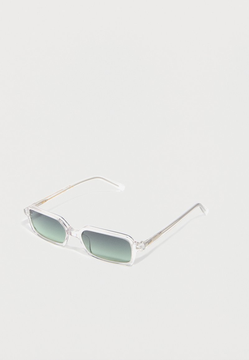 Διάφανα ορθογώνια γυαλιά ηλίου με φακούς σε πράσινη απόχρωση, λεπτοί διάφανοι βραχίονες, τοποθετημένα πάνω σε μία λευκή επιφάνεια.