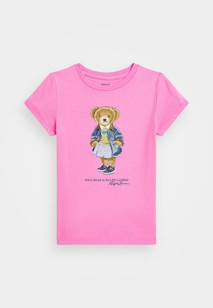 Růžové bavlněné tričko s potiskem kreslené medvěda v džínové bundě a kostkované sukni, design s nápisem "Polo Bear od Ralph Lauren" pod obrázkem.
