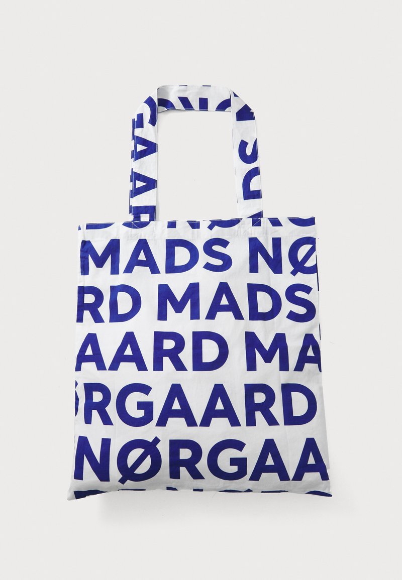 Tote Bag mit blauer Schrift auf weißem Stoffhintergrund, mit sich wiederholenden Buchstaben, die "MADS NØRGAARD" buchstabieren. Rechteckige Form mit zwei Tragegriffen.
