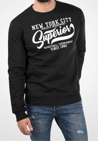 Czarna bluza z białym napisem „New York City Athletic Department Superior Basketball Tournament Since 1982”. Mankiety i dół wykończone ściągaczem.