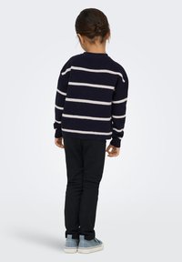 Pull rayé marine avec des rayures blanches, pantalon noir et chaussures bleues. Le pull a une coupe décontractée, un col rond et des poignets côtelés.