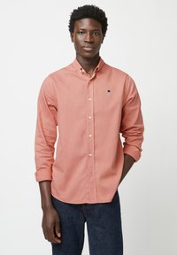 Lichtroze knoopshirt met een kraag, lange mouwen opgerold tot de ellebogen, en een klein blauw logo op de borst. Draag het met donkere denim jeans.