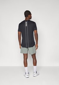 T-shirt atlético preto com logótipo "BORG" branco e riscas verticais nas costas, combinado com calções verde-claro e ténis brancos.
