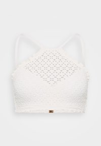 Biela čipkovaná podprsenka s vysokým výstrihom, tenkými nastaviteľnými ramienkami a vzorom kvetinových výrezov. Obsahuje zakrivené okraje a malý kovový štítok.