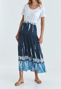 Falda larga y de capas en azul marino con patrones de teñido anudado en blanco y azul claro. Combinada con una camiseta de algodón blanca y sandalias en tono bronceado.