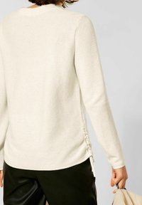 Maglia a maniche lunghe in tessuto cremoso con texture, caratterizzata da un tessuto a coste, dettagli arricciati sui lati e scollatura rotonda, abbinata a pantaloni in pelle nera.