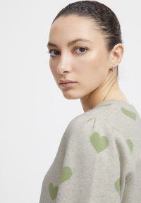Pull gris clair avec des motifs de cœurs verts, texture douce, encolure ronde et légères fronces aux coutures des épaules.