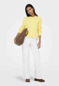 Rumeno gumbno jopico, bele široke hlače, rjava usnjena torbica in rjavi čevlji. Mehak material z gladko teksturo.