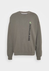 Sudadera verde aceituna hecha de material suave, con cuello redondo, puños acanalados y texto negro vertical con un pequeño logo verde.