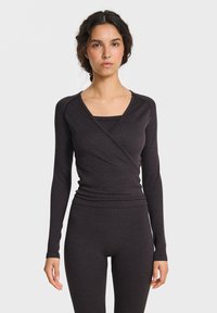 Dunkelgraues langärmeliges Wickeloberteil mit V-Ausschnitt und figurbetontem Design, kombiniert mit passenden hoch taillierten Leggings. Weicher, elastischer Stoff.